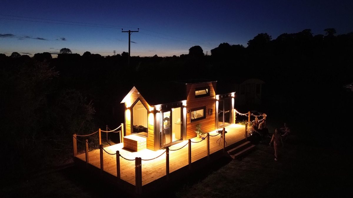 Tiny House at Flint Hall — timber-clad with deck, lit at dusk